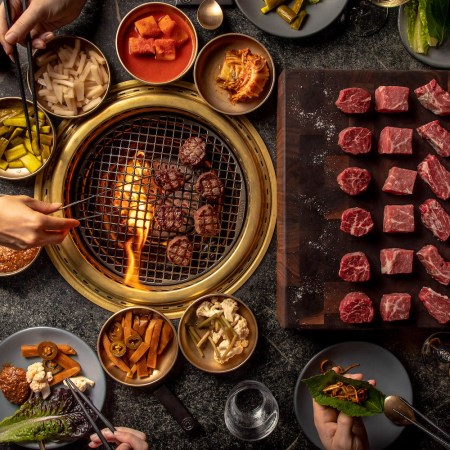 a tabletop grill at a korean steakhouse with marbled beef and banchan