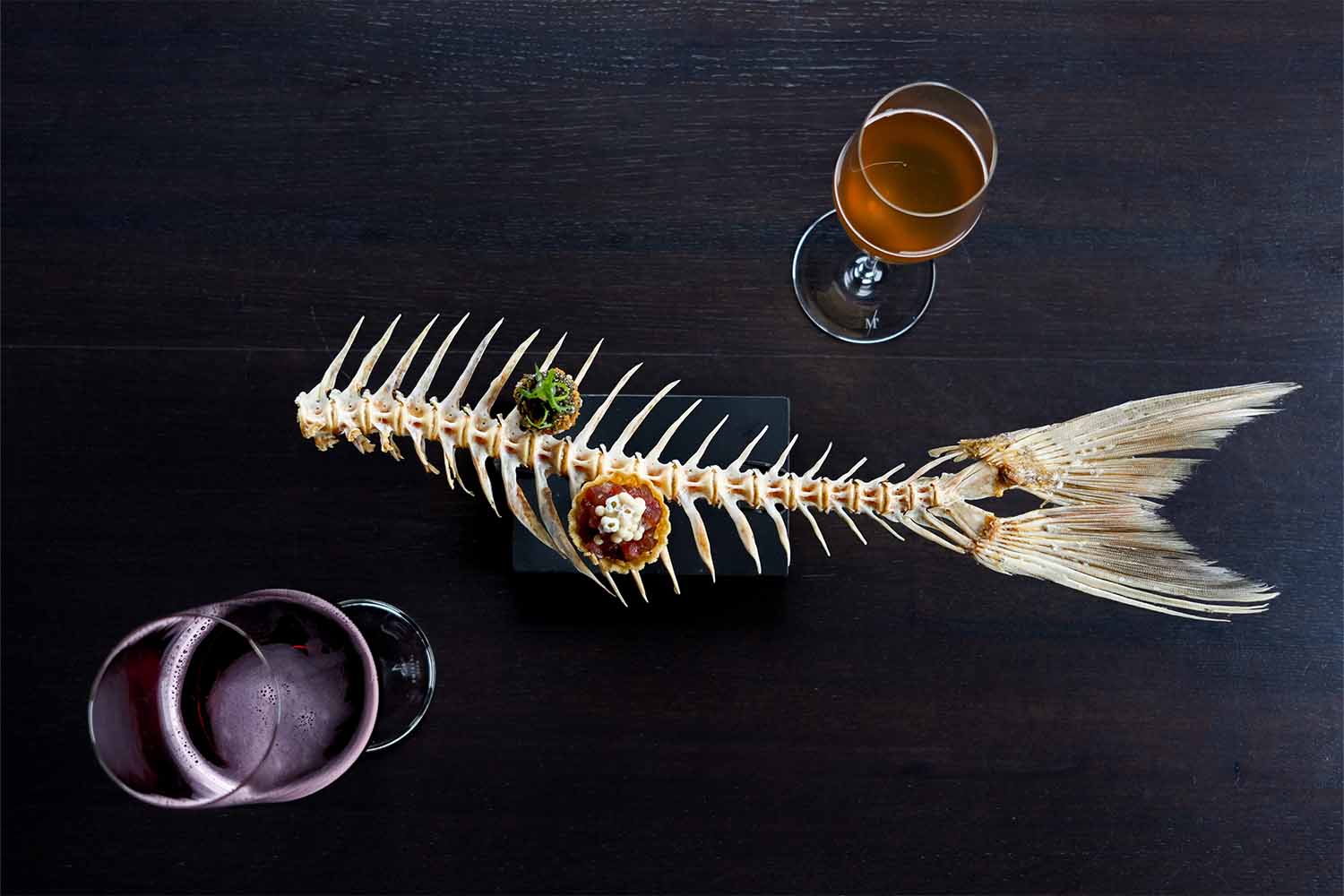 A fishbone serving platter with two hors d'oeuvres and two beers