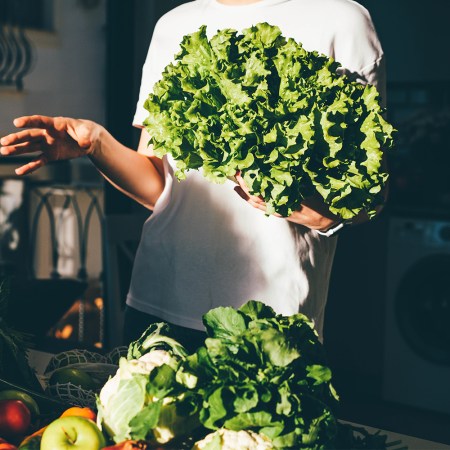 Person holding a large bunch of leafy greens, surrounded by fresh vegetables on a kitchen counter
