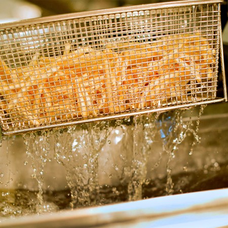French fries being lifted from a deep fryer filled with hot cooking oil