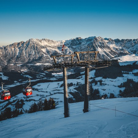 Red gondolas on a snow-covered slope at SkiWelt, Austria, on a clear winter's day.