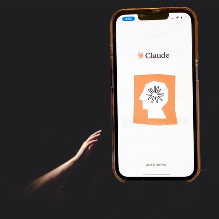 A hand reaching through darkness to a large iPhone depicting an AI logo on a backlit screen.
