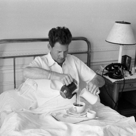 Man in bed pouring coffee and milk simultaneously with both hands