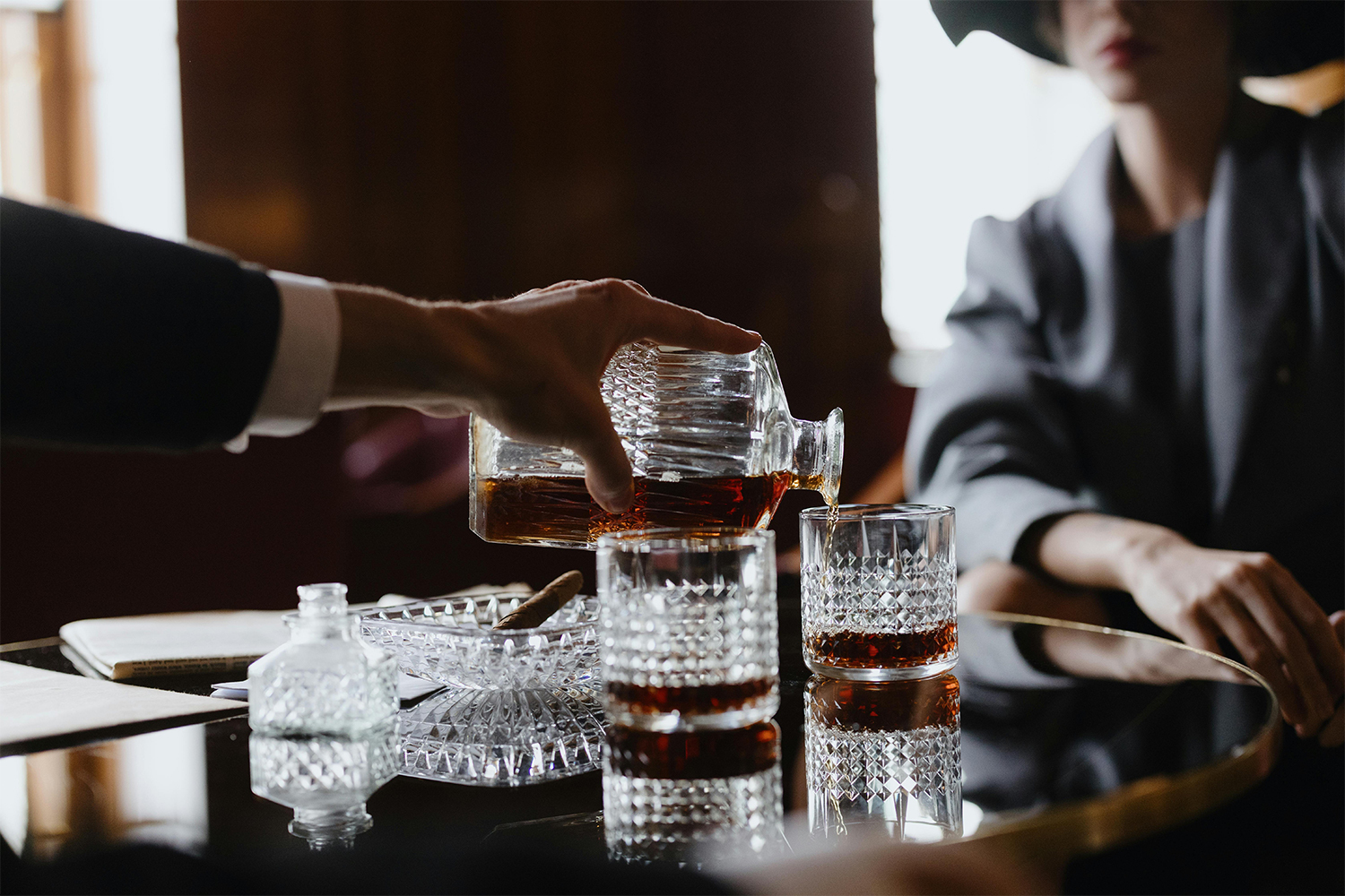 A person pouring whiskey into two different glasses for a woman