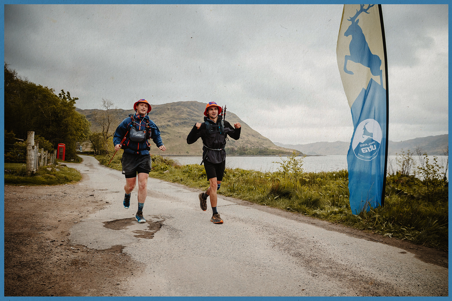 Two runners finish the Highland Ultra under a race flag.