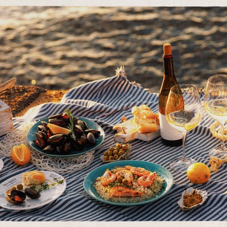 Table full of seafood and vegetable dishes and wine with the beach in the background
