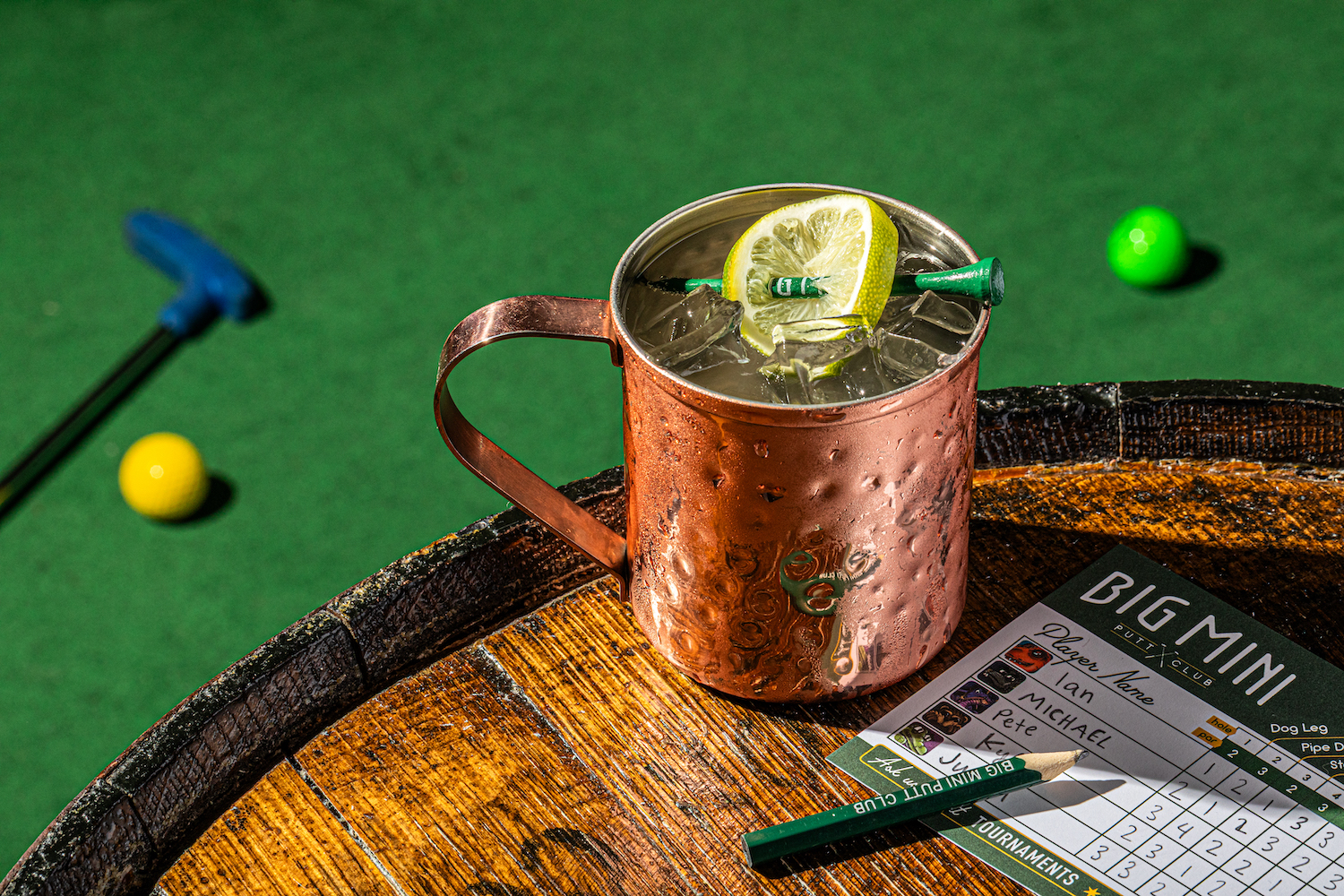 a mule cocktail sitting on top of a wooden barrel at a mini golf course