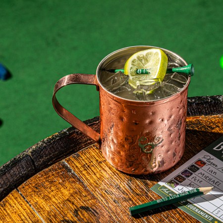 a mule cocktail sitting on top of a wooden barrel at a mini golf course