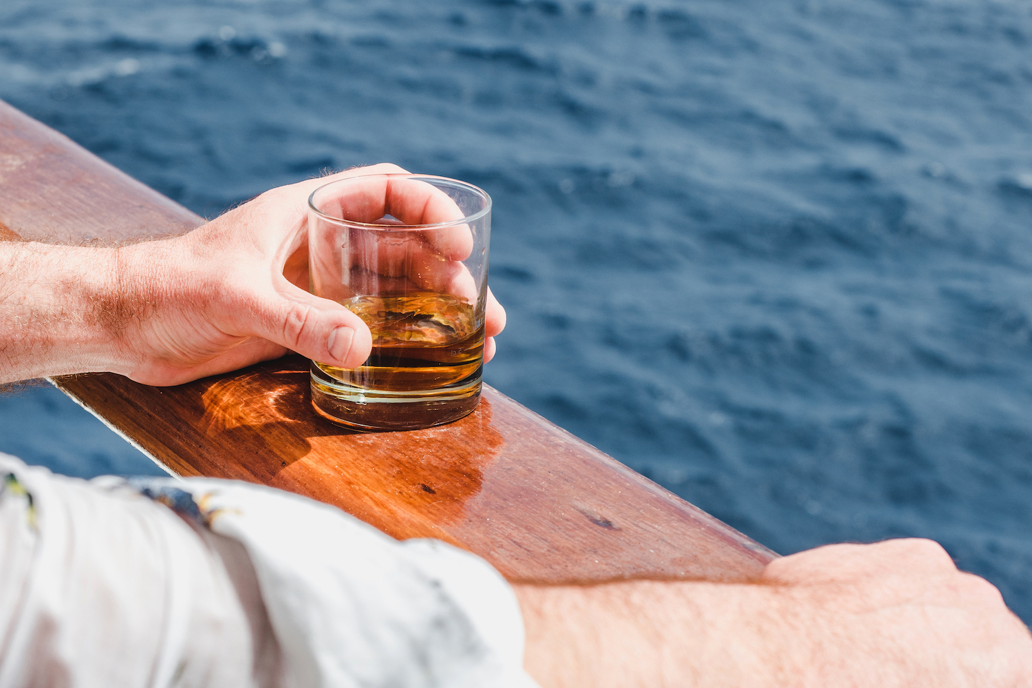 A hand holding a glass of whiskey with water in the background