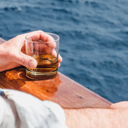 A hand holding a glass of whiskey with water in the background