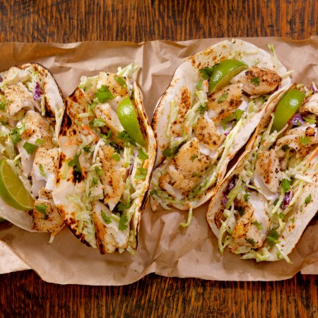 Grilled Fish Tacos with Creamy coleslaw, Lime and Fresh Cilantro on brown paper on a wooden table