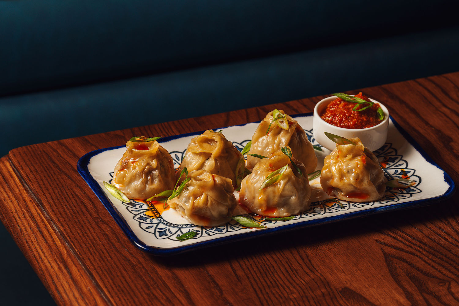 Pork and vegetable Tibetan momos with raw garlic-tomato on a white plate on a wooden table