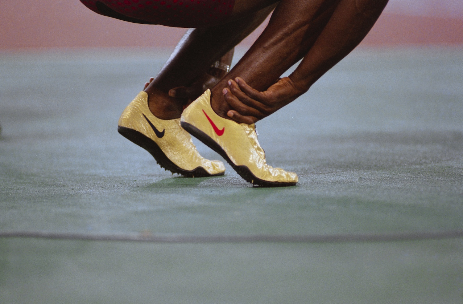 Close-up of powerful ankles in motion during a dynamic warm-up, wearing gold Nike spikes on a track surface.