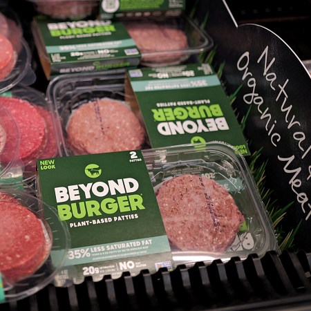 A grocery store display with Beyond Burger and Impossible Burger patties next to a sign that says "Natural & Organic Meat"