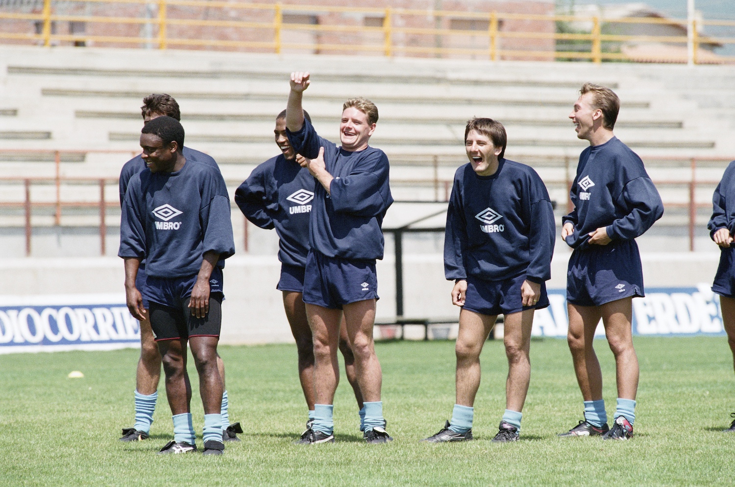 Group of soccer players in vintage Umbro training gear laughing and smiling during practice on a sunny field