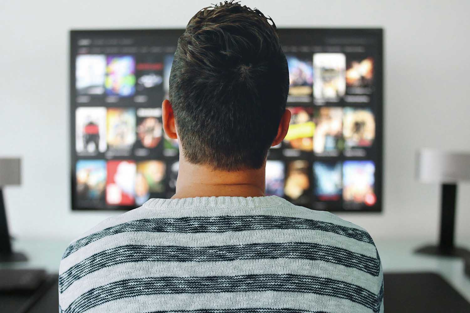 Young man staring at large TV screen full of movie choices