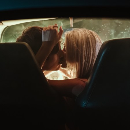 Young couple kissing each other while sitting inside vintage car at night