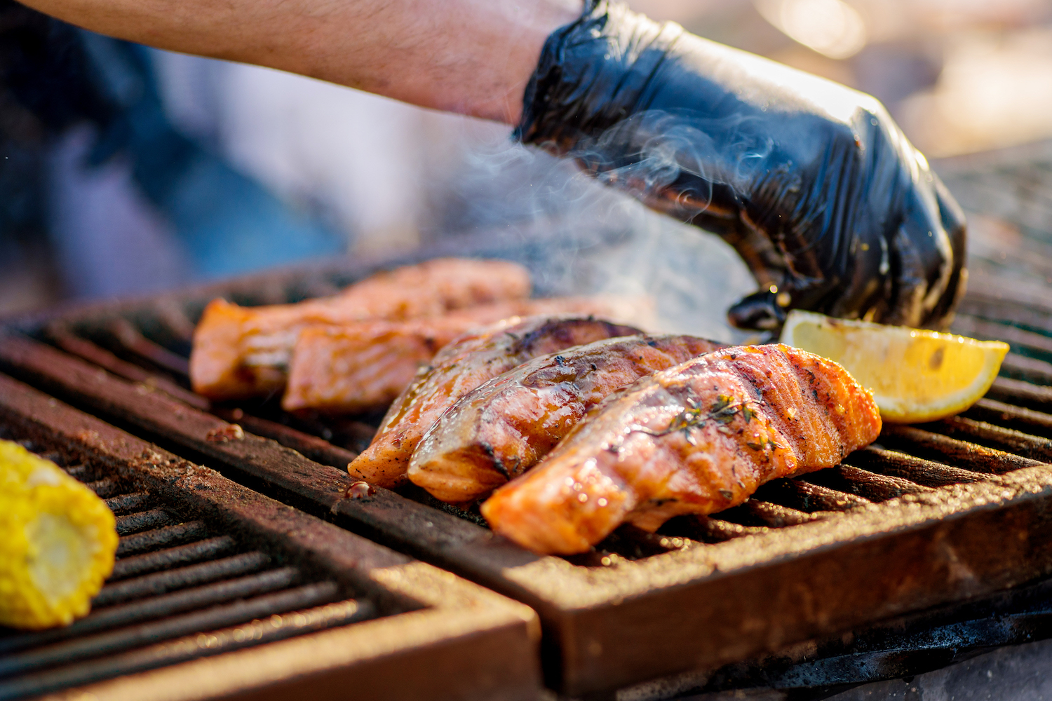 Gloved hands turn pieces of fish on the grill. Grilled salmon on a charcoal grill.