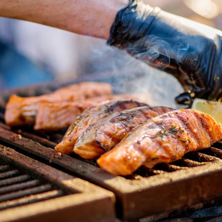 Gloved hands turn pieces of fish on the grill. Grilled salmon on a charcoal grill.