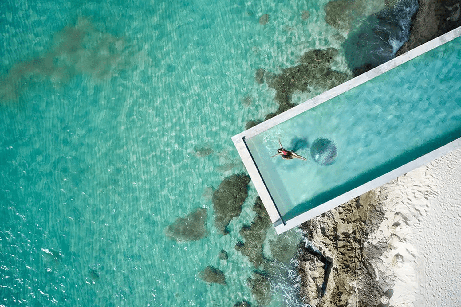 a woman floating in an infinity pool above the caribbean sea