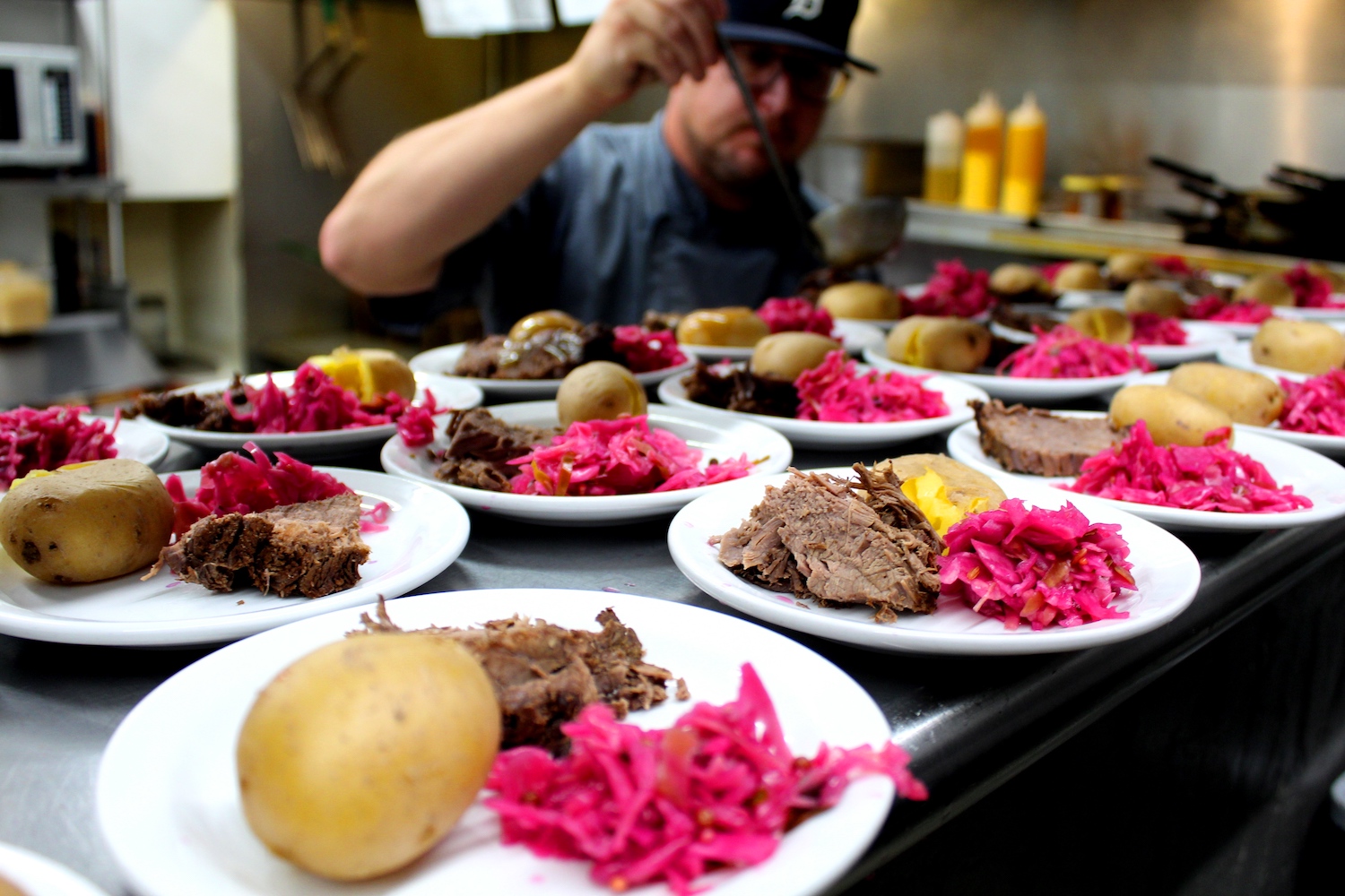 meat, cabbage and potatoes being plated by a chef on white plates