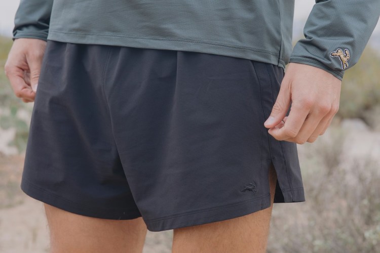 a cropped photo of a model in blue running shorts and a green long sleeve shirt