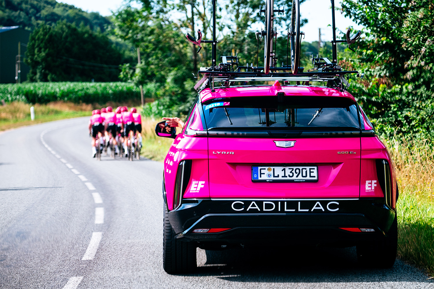 An electric Cadillac Lyriq in a pink livery following cyclists from the EF Education-EasyPost team