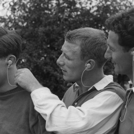 Three men wearing vintage-style wired headphones, smiling and interacting outdoors in a retro black-and-white photo.