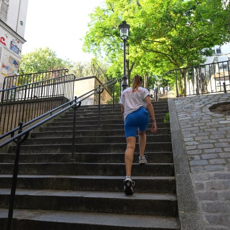 A woman in athletic clothing climbs an outdoor city staircase, showcasing strong posture and gait.