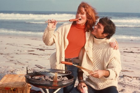 A man and woman enjoying a grilled hot dog on the beach.