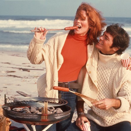 A man and woman enjoying a grilled hot dog on the beach.