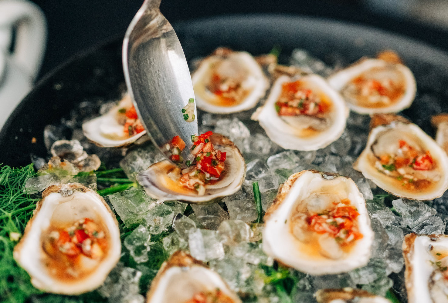 a spoon placing a red mignonette on oysters