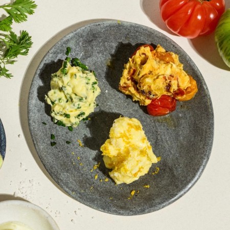 three compound butters on a grey plate on a table next to fresh produce