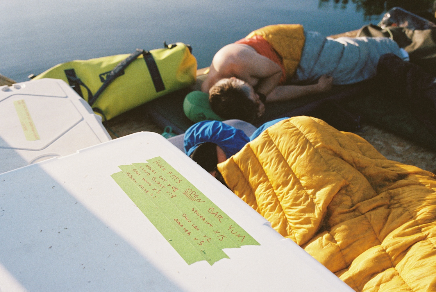 A close-up of the raft's coolers, with a man on a sleeping bag in the background.