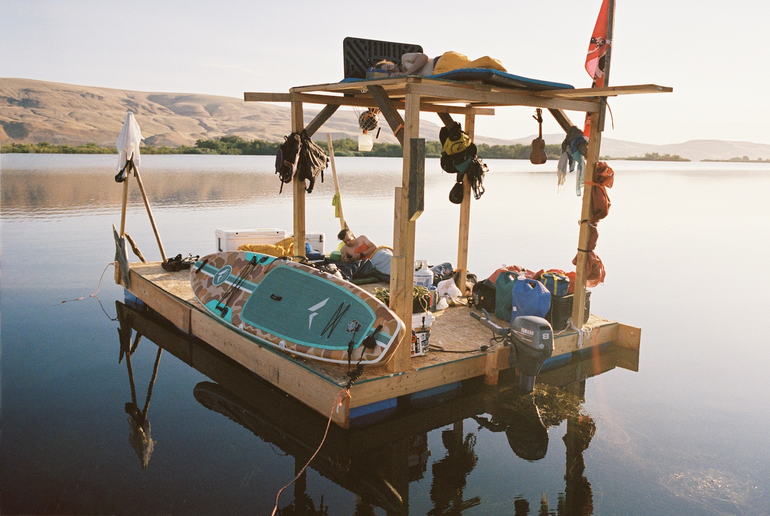 A full view of the DIY raft, with multiple levels, bags, coolers, a paddleboard and a propane tank.