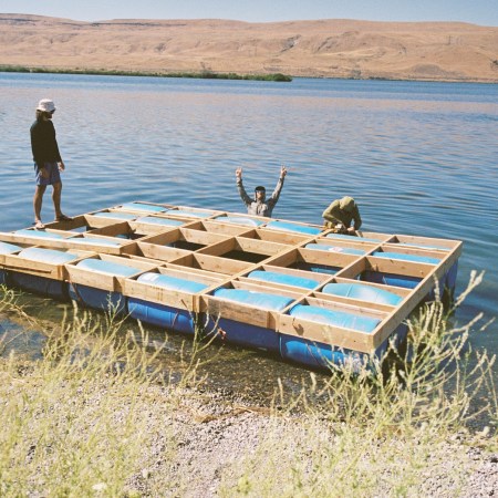 A trio of men loading a makeshift catamaran into a river.