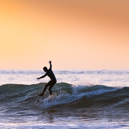 A surfer balancing on one leg while riding a wave at sunset.