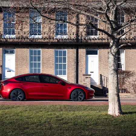 A red Tesla Model 3 sitting in front of a house. New data shows the EV is the least-stolen car in the U.S.