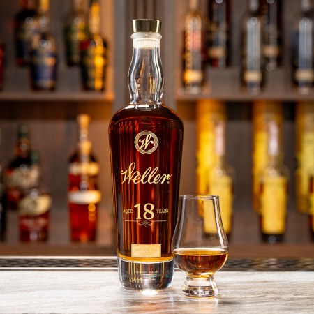 A bottle of Weller 18 Year Old sitting on a bar next to a small glass of the whiskey