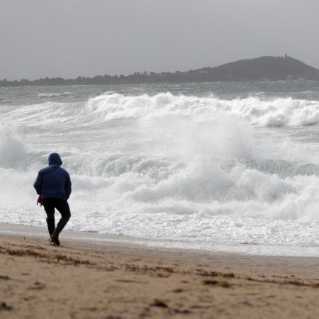 A man walks on a beach in winter, watching the waves.