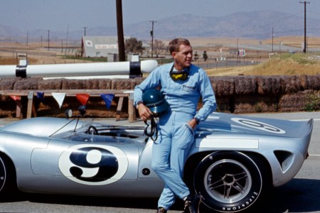 Steve McQueen with a racing car behind him