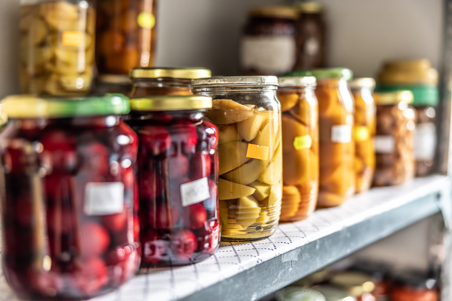 Homemade fruit and vegetable preserves in glass jars on a shelf in the pantry