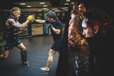 Left: An MMA coach wearing focus mitts and pads spars with a fighter in the cage. Right: A coach leans up against the cage watching his fighters.