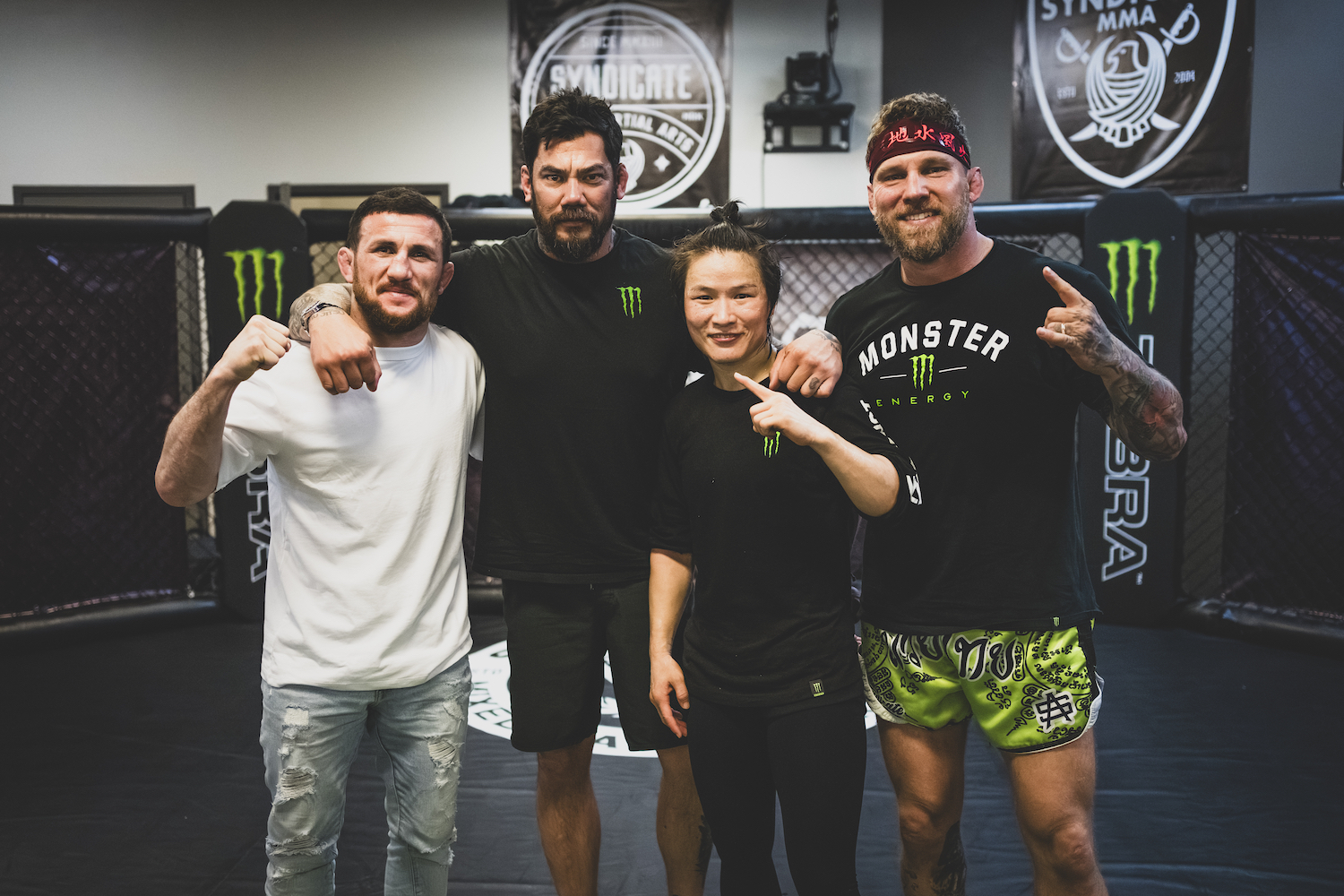 Two male MMA fighters and a female MMA fighter standing next to their coach in the middle of a ring