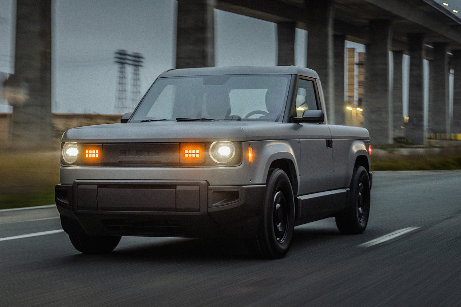 The Slate Truck, an electric pickup backed by Jeff Bezos, driving down the road with its headlights on