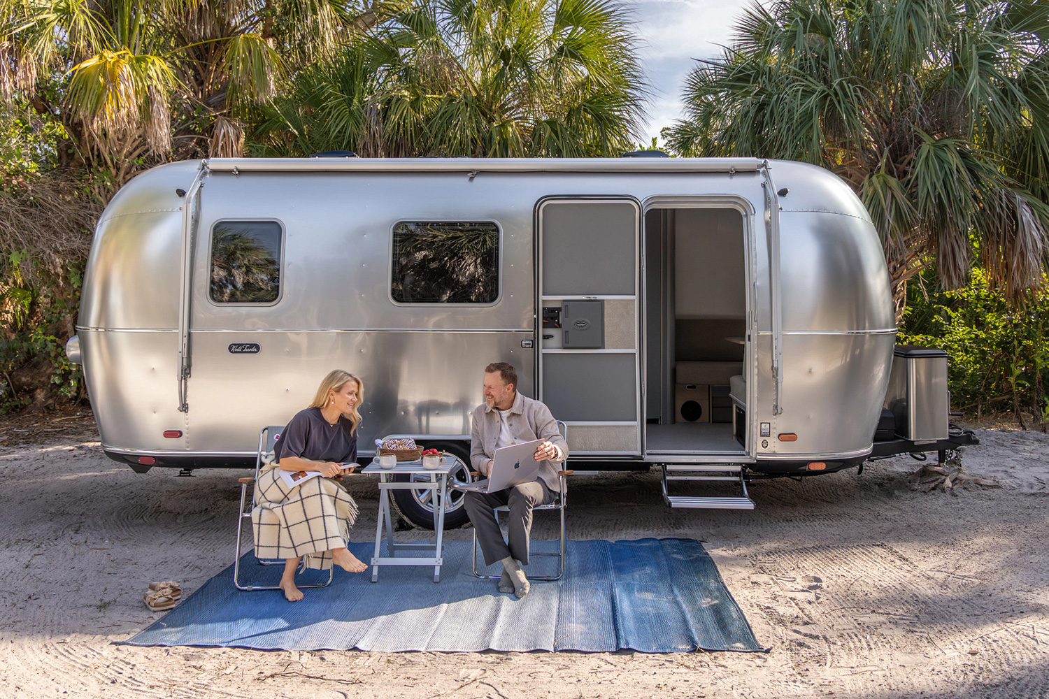 A man and woman sitting outside the Airstream World Traveler 22RB, a new, more affordable silver bullet travel trailer from the RV company