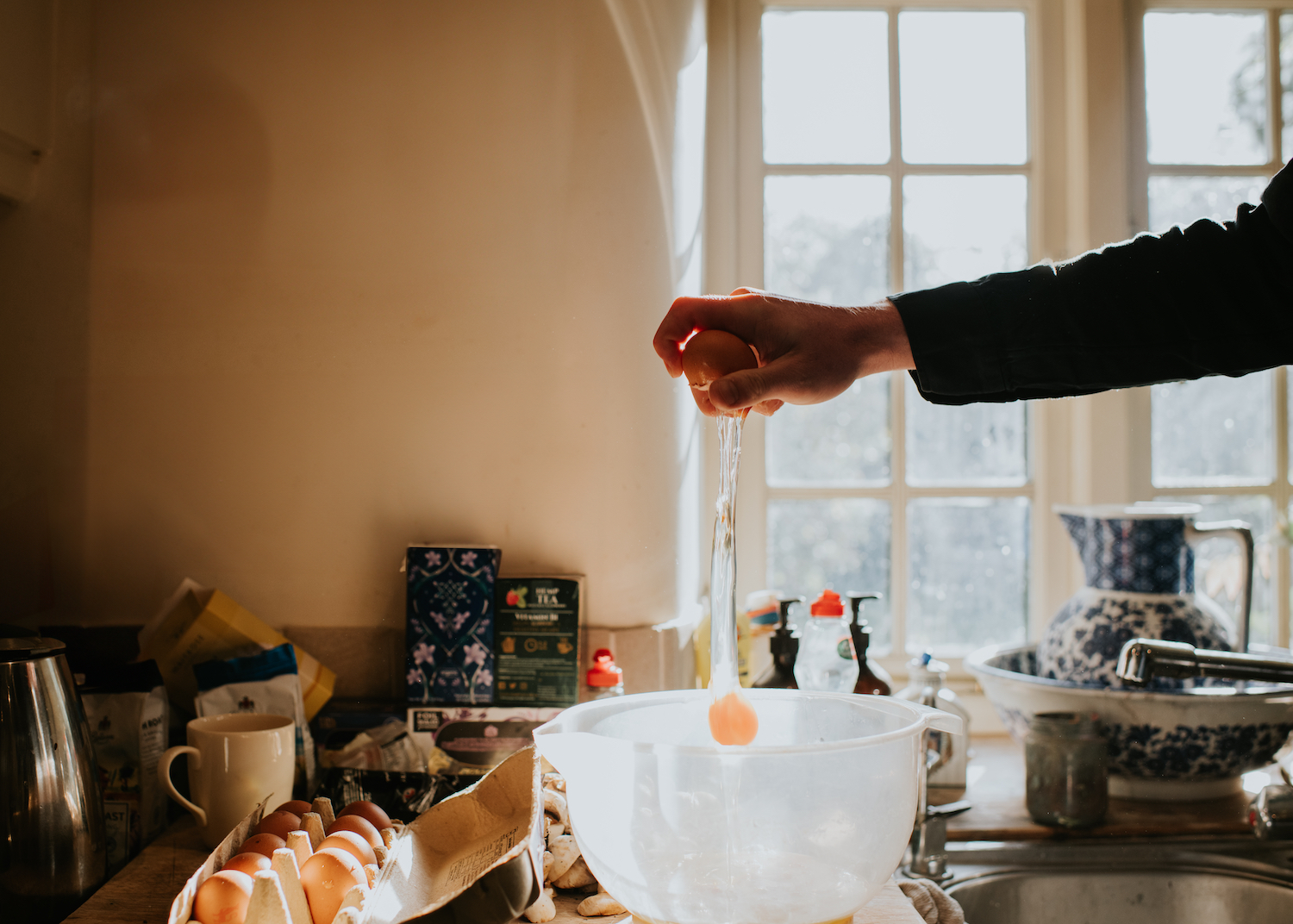 A man breaks an egg into a mixing bowl from a height, using one hand.