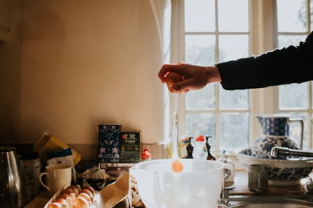 A man breaks an egg into a mixing bowl from a height, using one hand.