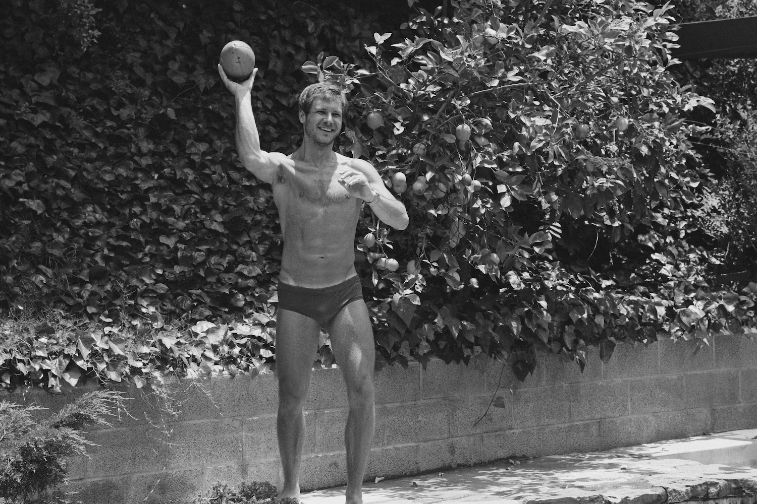 Harrison Ford standing in his underwear, throwing a football.