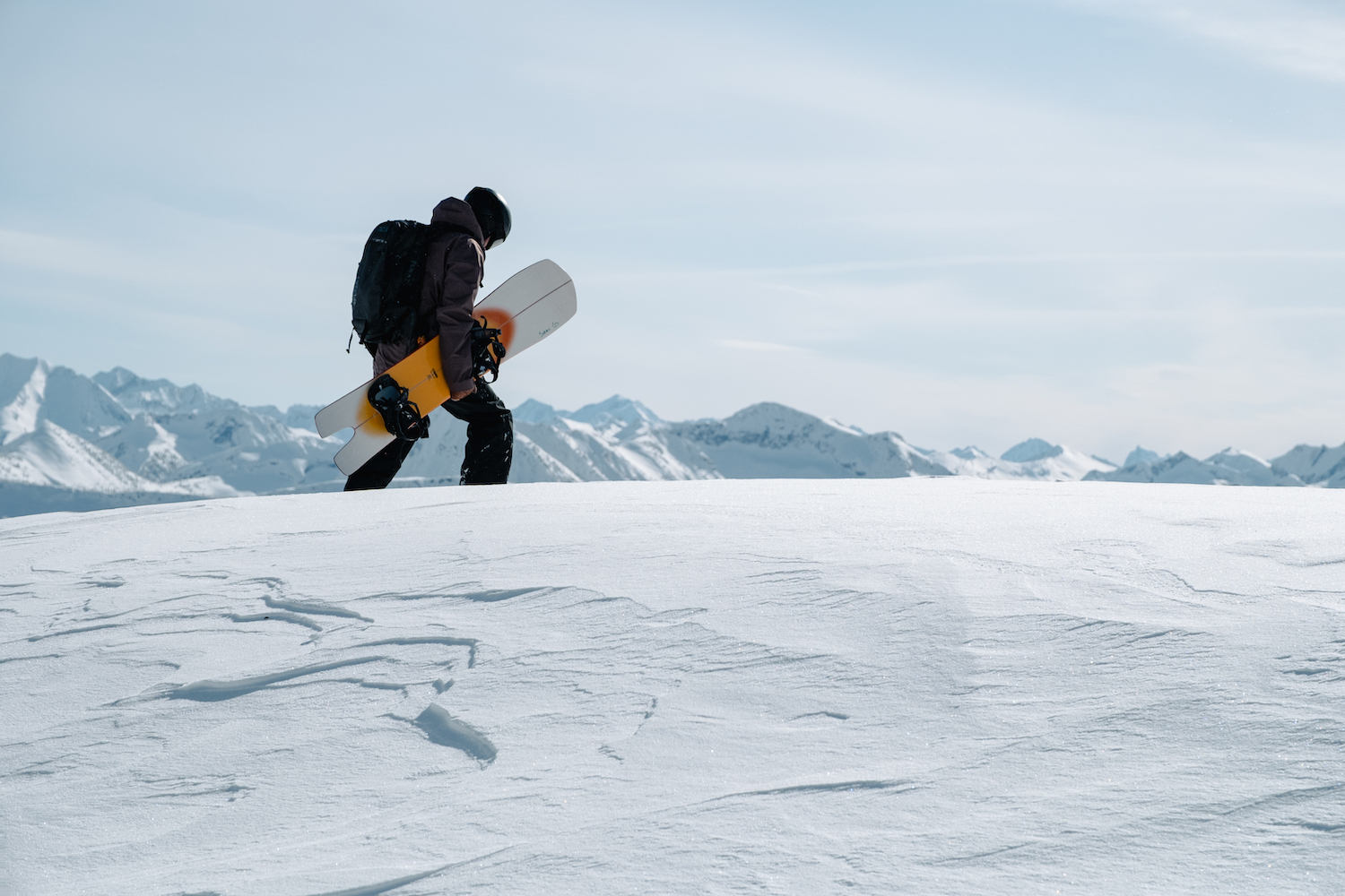 A man carrying a snowboard walking through snow.